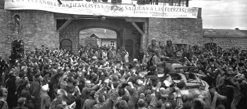 Prisioneros de Mauthausen saludan a la 11ª División Acorazada de EE.UU. por su liberación bajo una pancarta escrita en español.