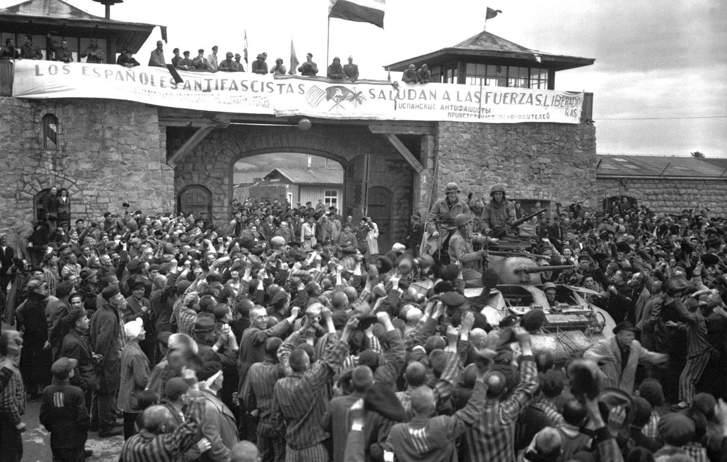 Prisioneros de Mauthausen saludan a la 11ª División Acorazada de EE.UU. por su liberación bajo una pancarta escrita en español.