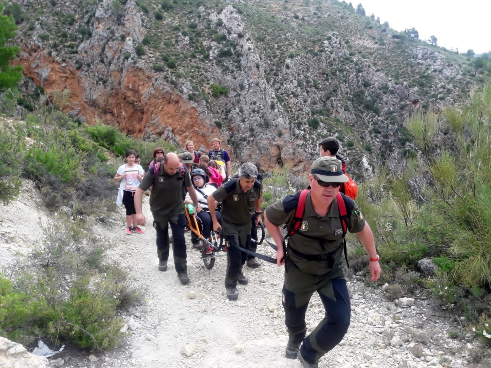 Los Agentes Medioambientales ayudando a practicar senderismo en silla de ruedas.