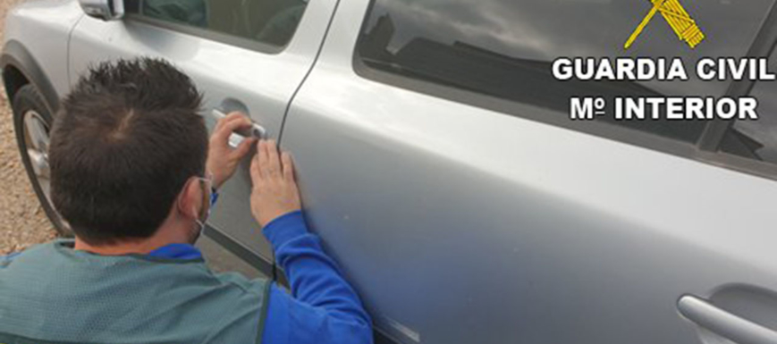 Un agente de la Guardia Civil inspecciona el bombín de una puerta de uno de los coches en los que robaron.