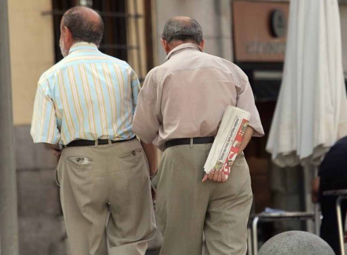 Dos mayores pasean por la calle con el periódico en la mano.