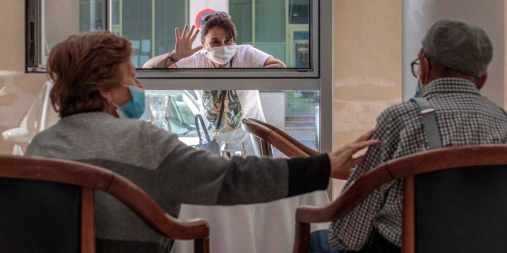 Un familiar saluda por la ventana a dos ancianos en una residencia de mayores.