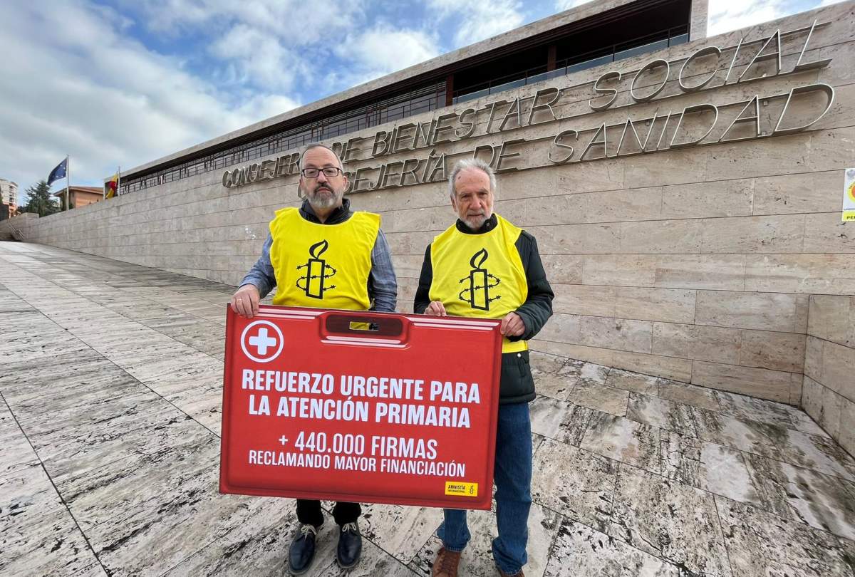 Dos miembros de Amnistía Internacional, con un botiquín rojo de cartón pluma de grandes dimensiones ante la Consejería de Sanidad.