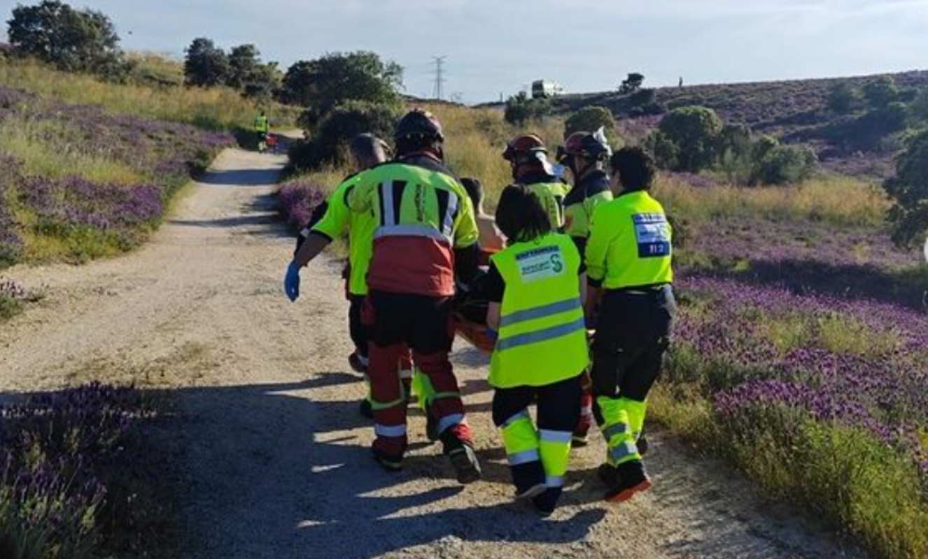 Los bomberos y los sanitarios portean al ciclista herido cerca del embalse de La Portiña.