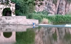 Un hombre y una mujer cruzando el Tajo por el azud cercano a la barca de pasaje.